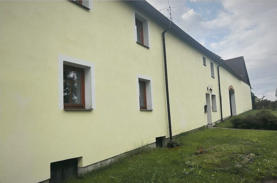 Dlouhá žlutozelená fasáda statku s okny a trávníkem