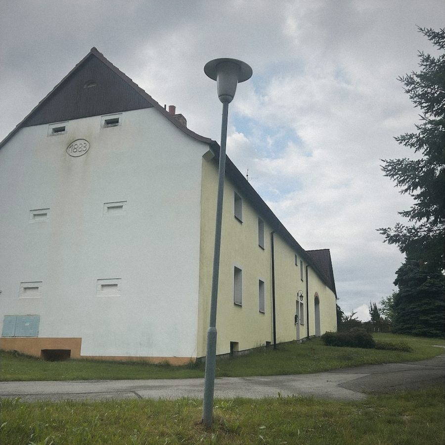 Dlouhá žlutozelená budova statku s tmavým štítem